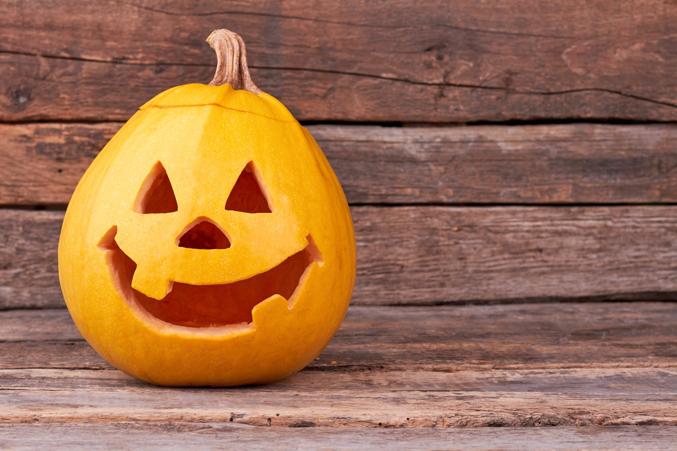 A photo of an orange jack-o-lantern (carved pumpkin) with a smiling face on a background of wood panels.