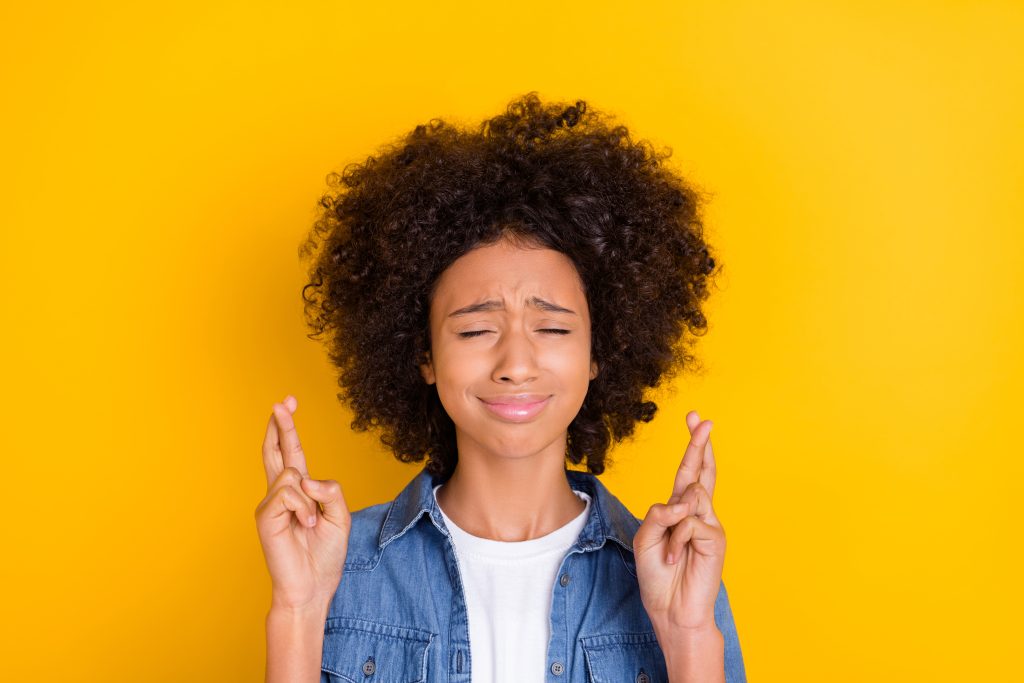 Portrait of woman with afro hair crossed fingers praying wait expect isolated over bright yellow color background.