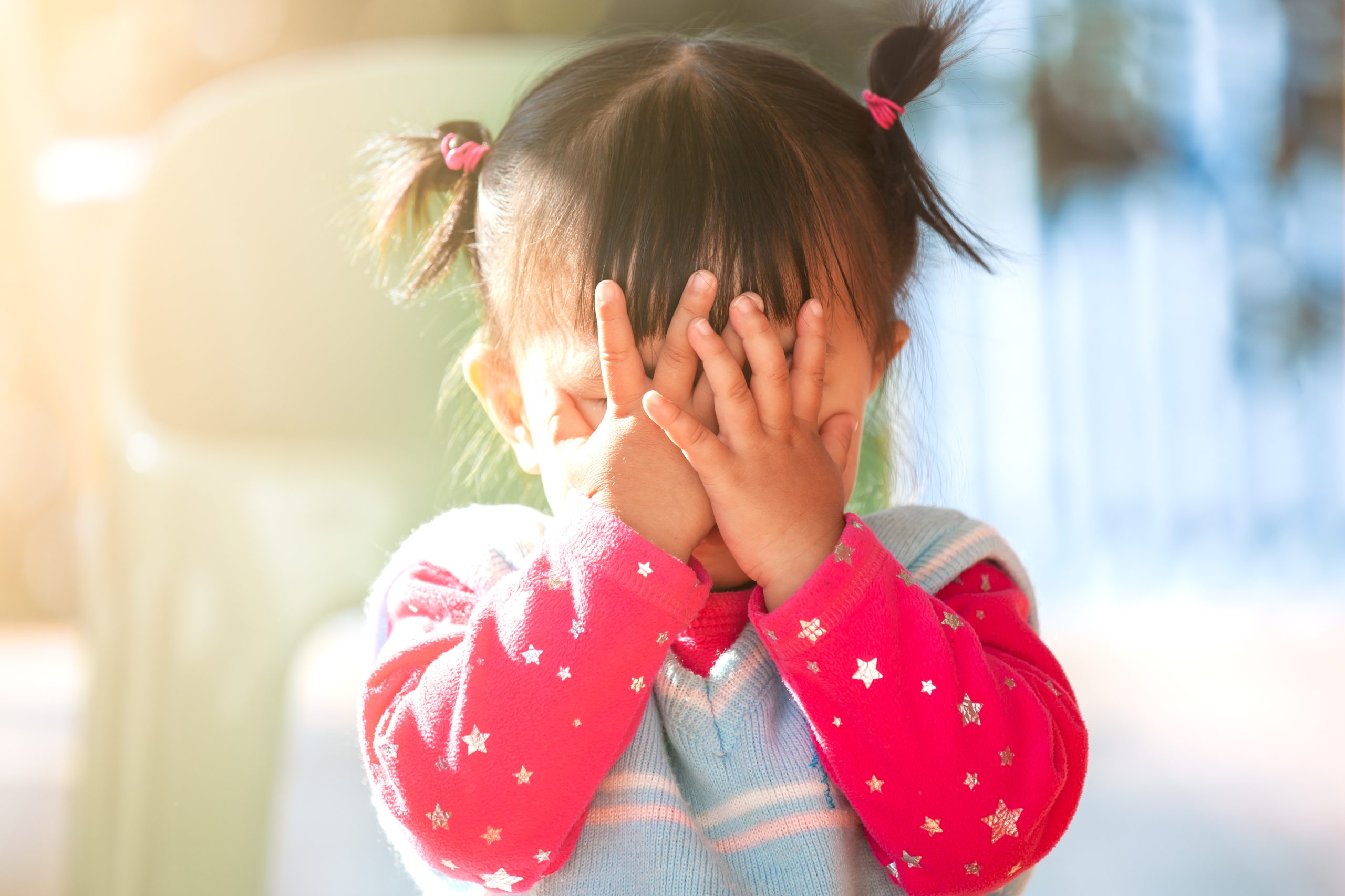 Cute asian toddler girl hiding her face behind her hands